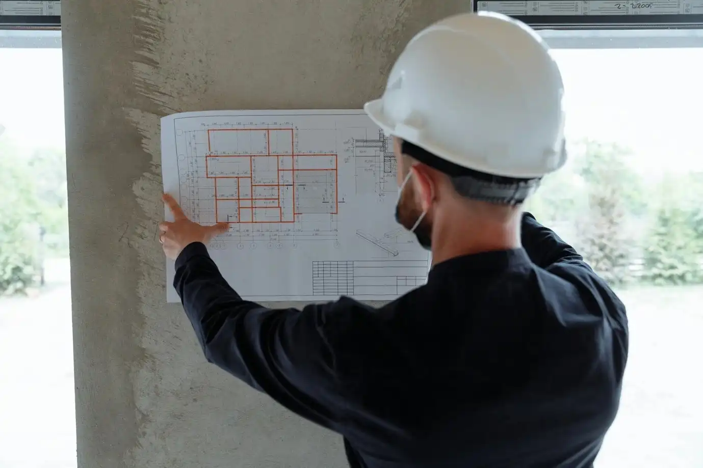 Backview of an engineer holding a floor plan on a wall