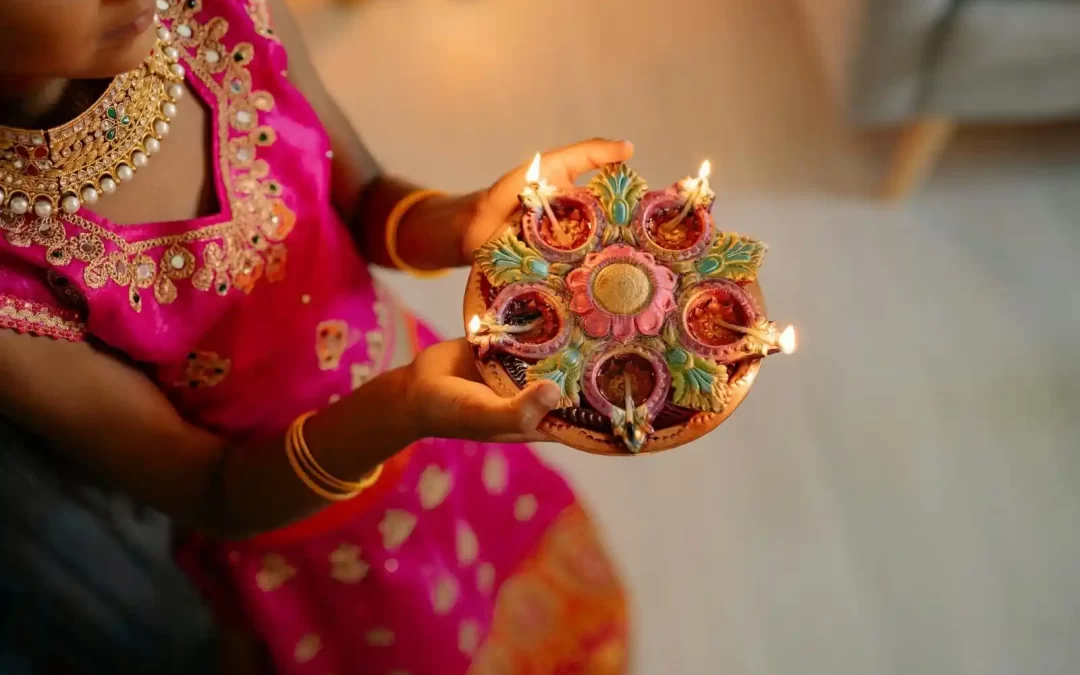 A girl standing with a plate filled with Diya’s for Diwali