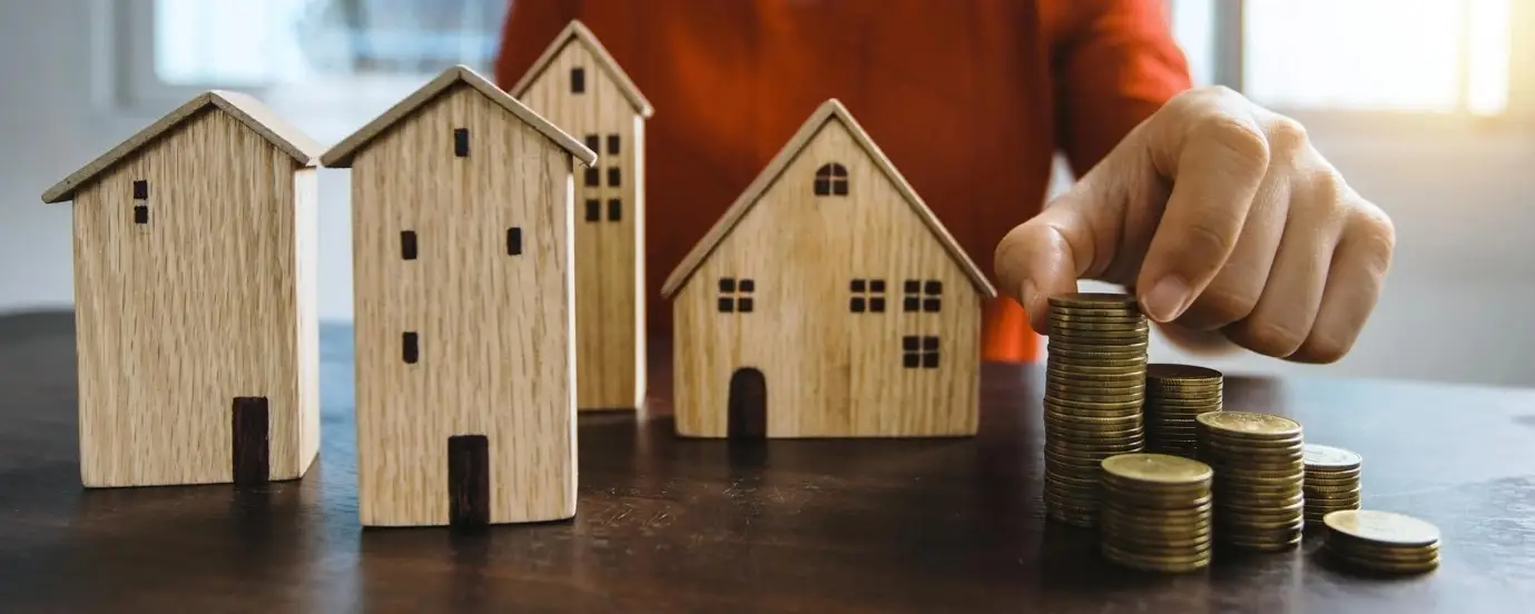 Brown wooden miniature houses with close up of hands stacking coins.