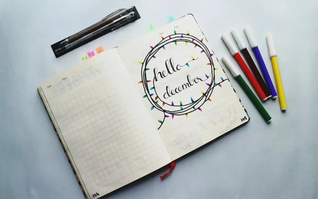 An open planner with “Hello December” written on its page