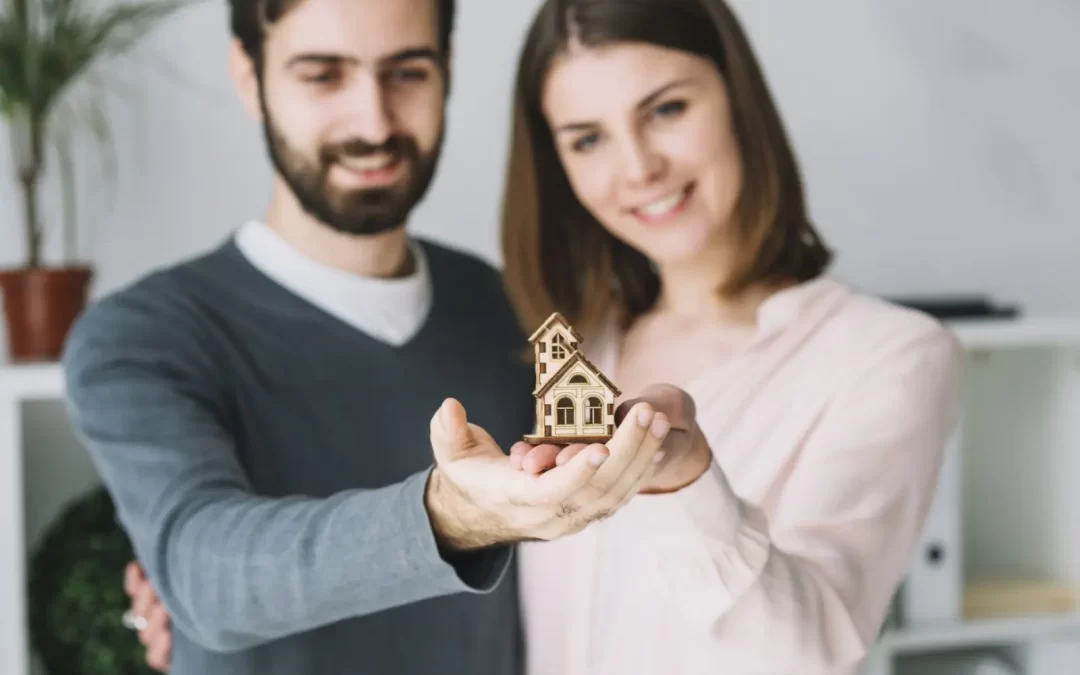 Couple holding a toy-sized house thinking about buying a home