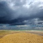 Monsoon beach scene near homes in Panjim with dramatic clouds over the ocean.